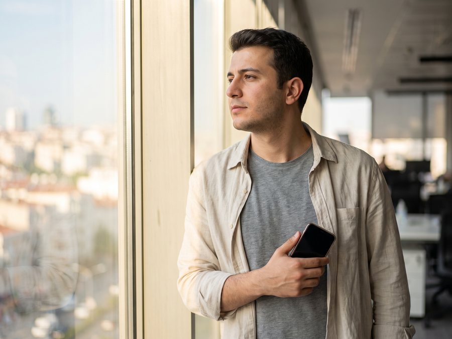 Ofis penceresinin önünde telefonunu tutan genç bir çalışan